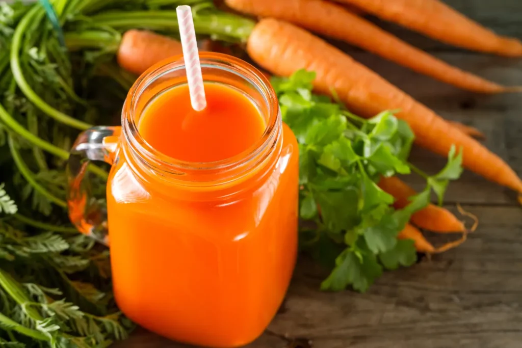 Fresh carrot juice surrounded by tropical fruits and carrots.