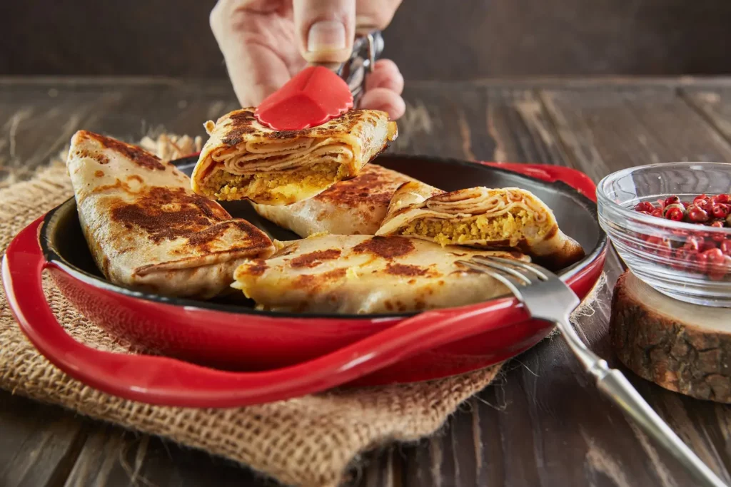 Platter of golden arayes with tahini sauce and garnishes on a wooden table.