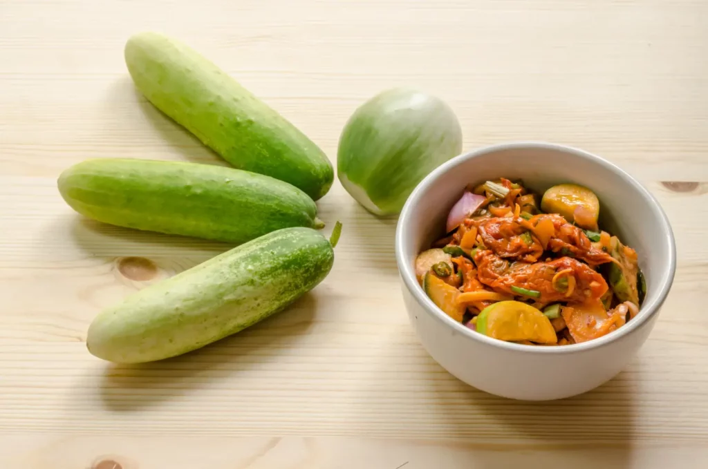 A bowl of cucumber kimchi surrounded by fresh ingredients.