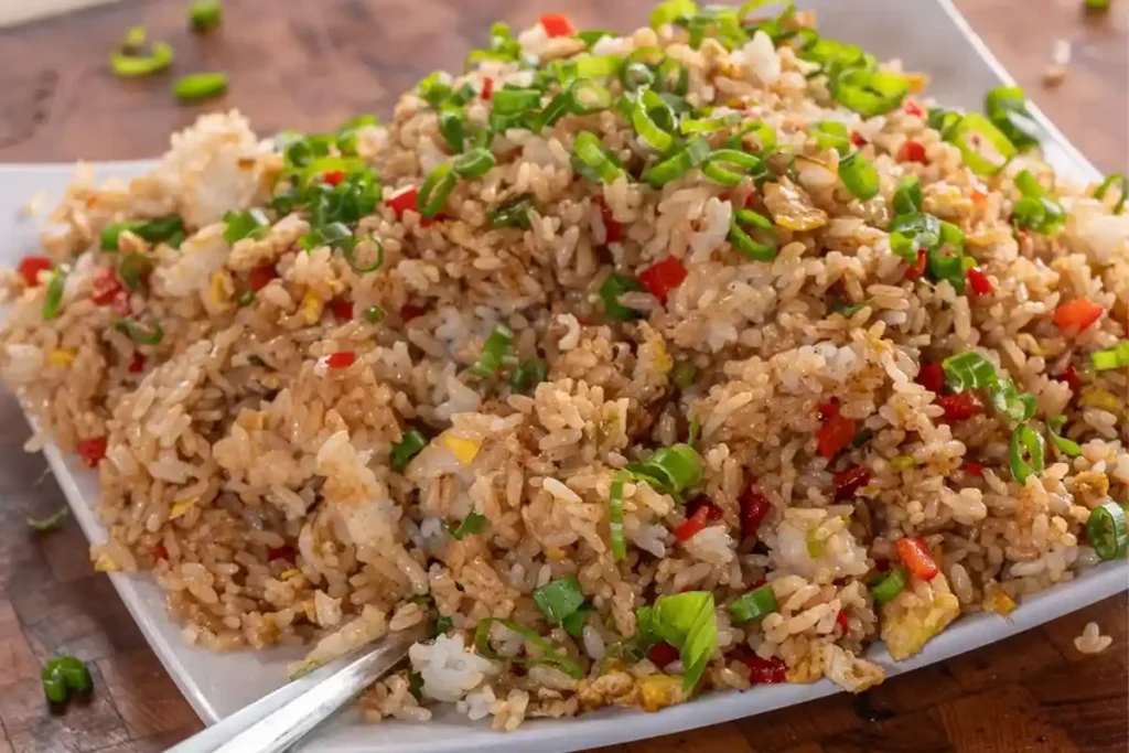 A plate of Blackstone fried rice garnished with fresh vegetables, featuring vibrant colors and rich textures, served on a rustic wooden table.