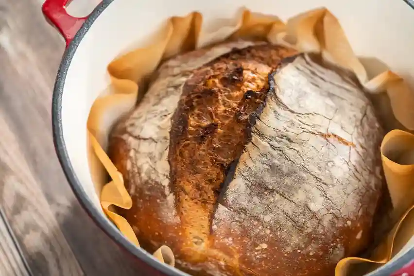 Freshly baked artisan bread in a Dutch oven with rosemary garnish