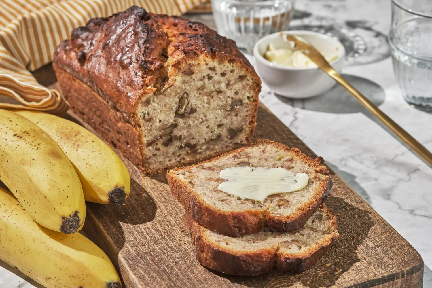 Freshly baked banana bread with 2 bananas on a wooden board