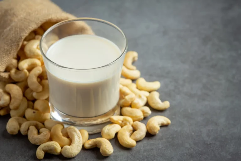 Homemade cashew milk in a glass jar surrounded by raw cashews and ingredients