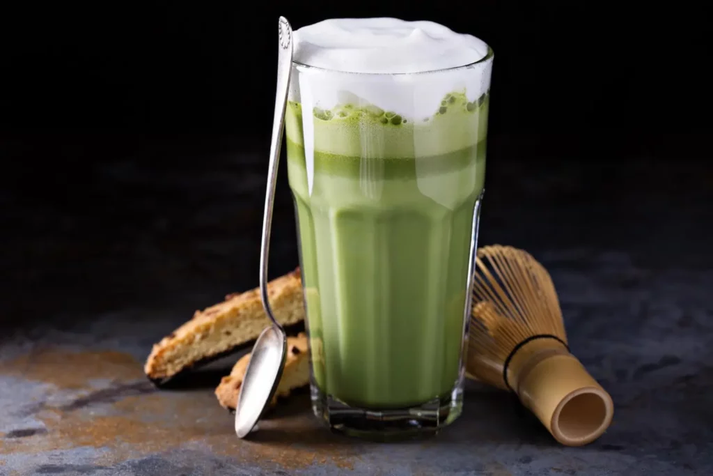 Layered iced matcha latte with bamboo whisk and matcha powder