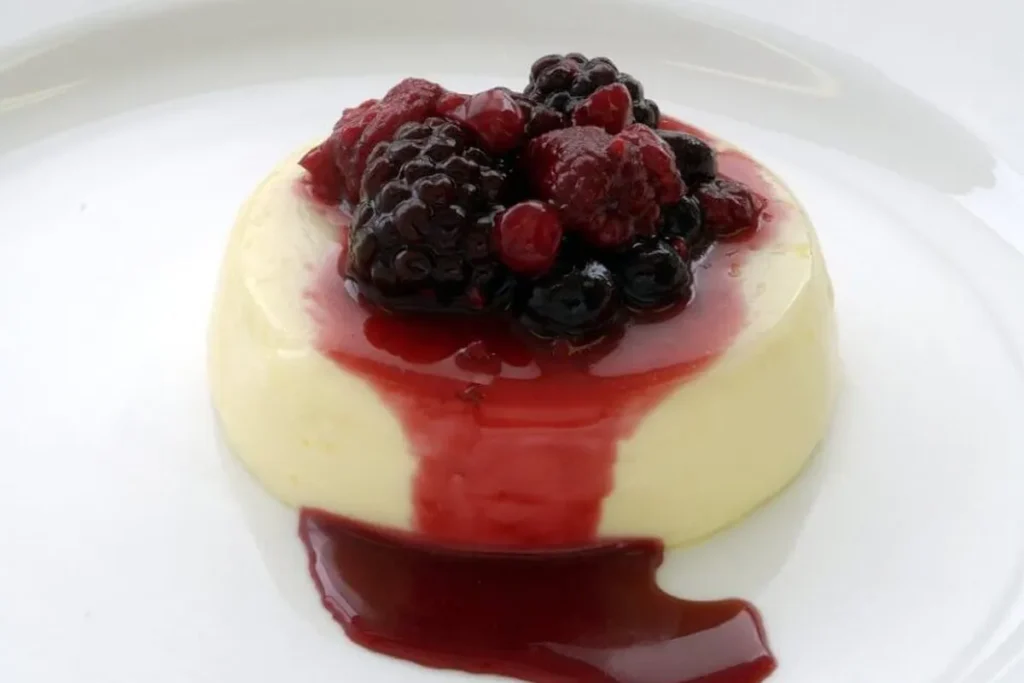 A creamy panna cotta topped with vibrant berry compote, served in a glass jar