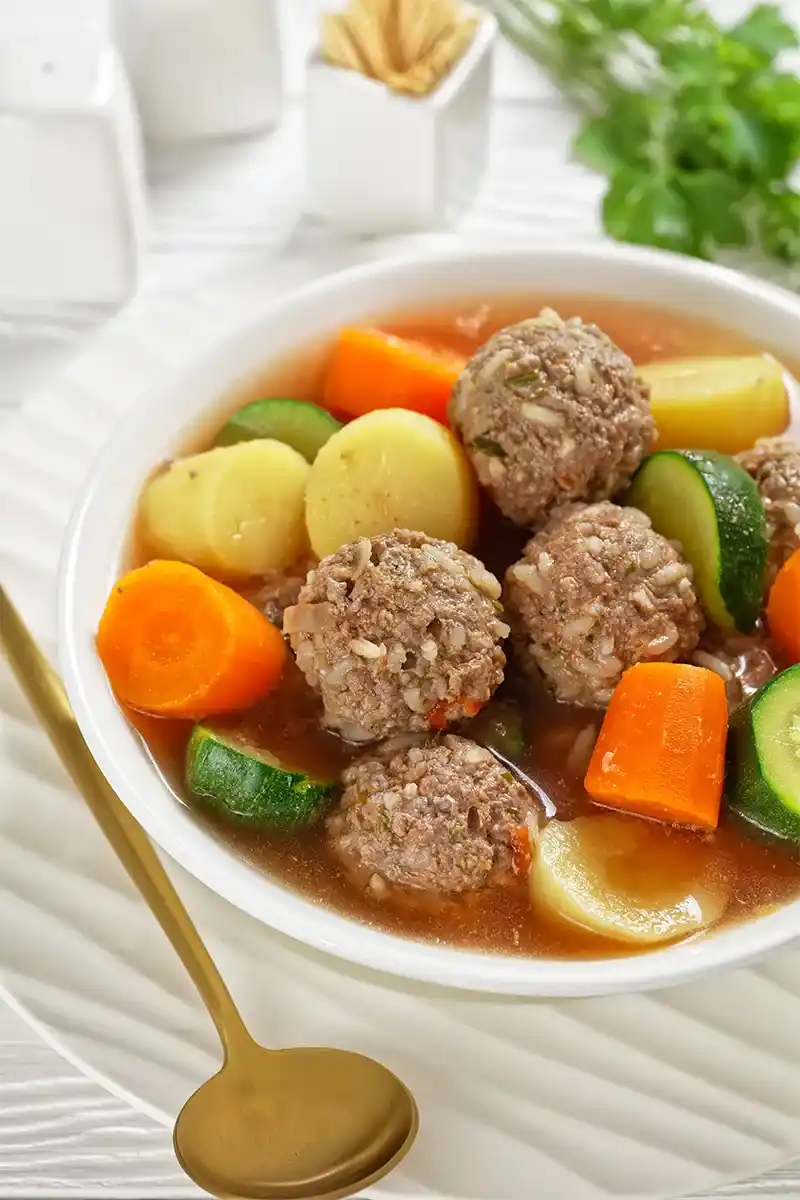 Raw albondigas meatballs being formed on a wooden board.