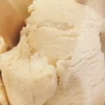 Creamy vanilla ice cream in a white bowl with one wooden spoon
